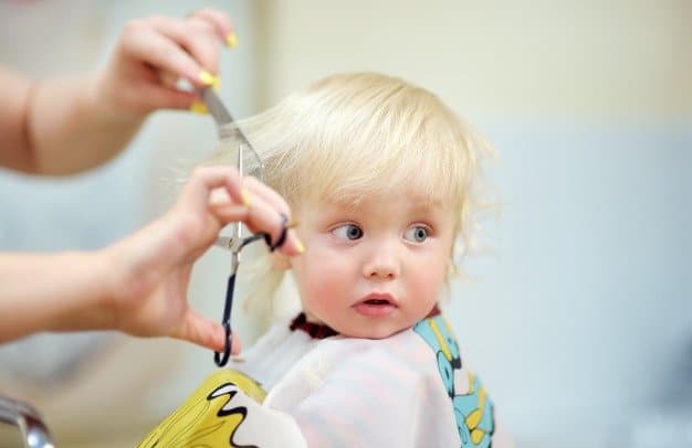Blonde haired toddler having a hair cut and facing towards the camera
