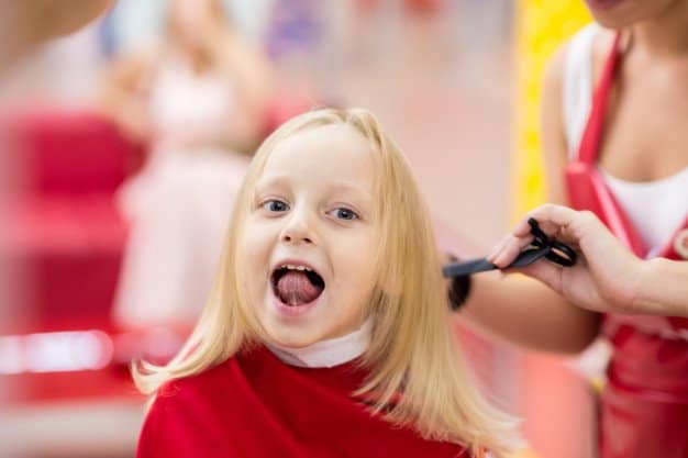 Cheeky young girl with long blonde hair getting hair cut