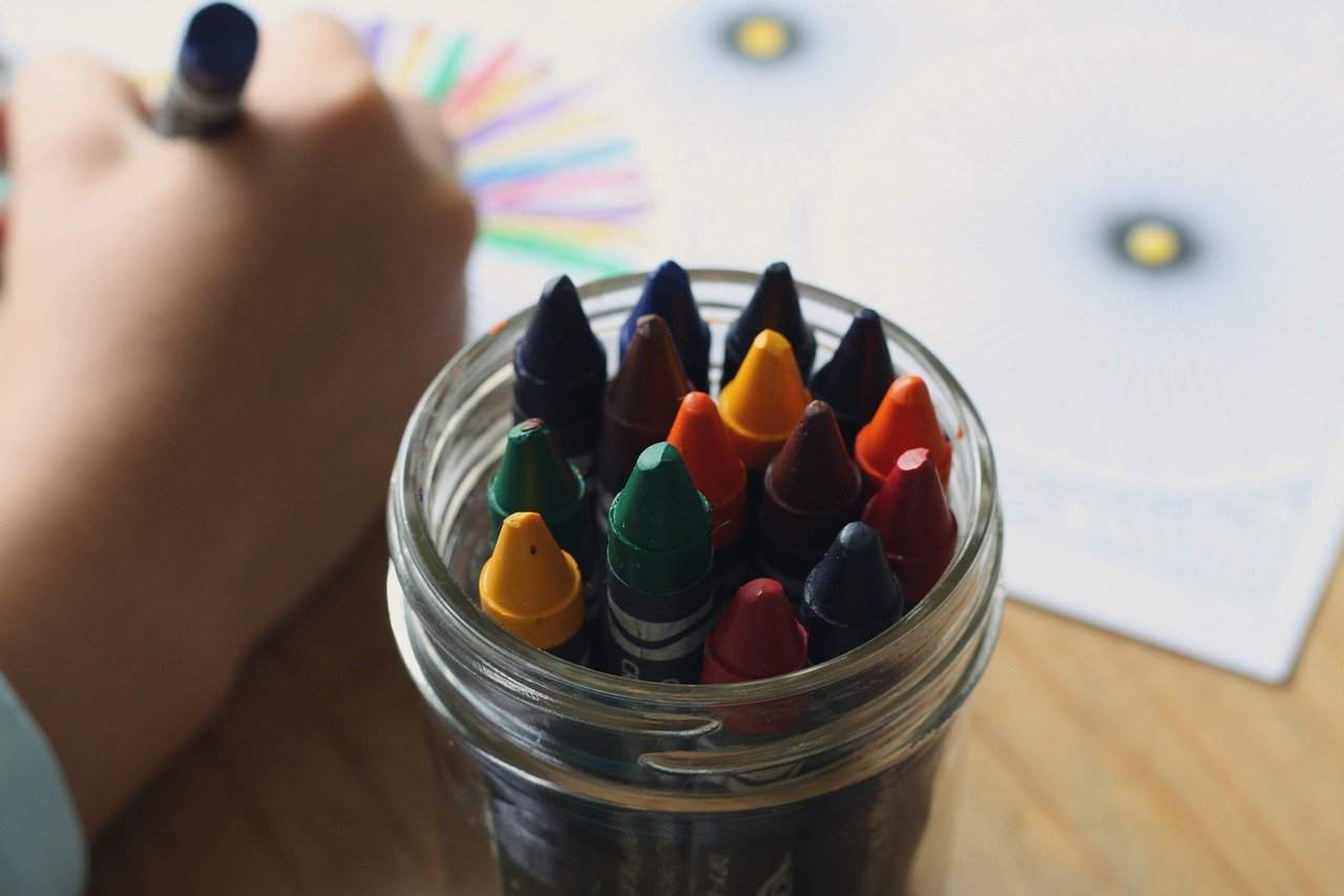 Jar of crayons and child's hand colouring