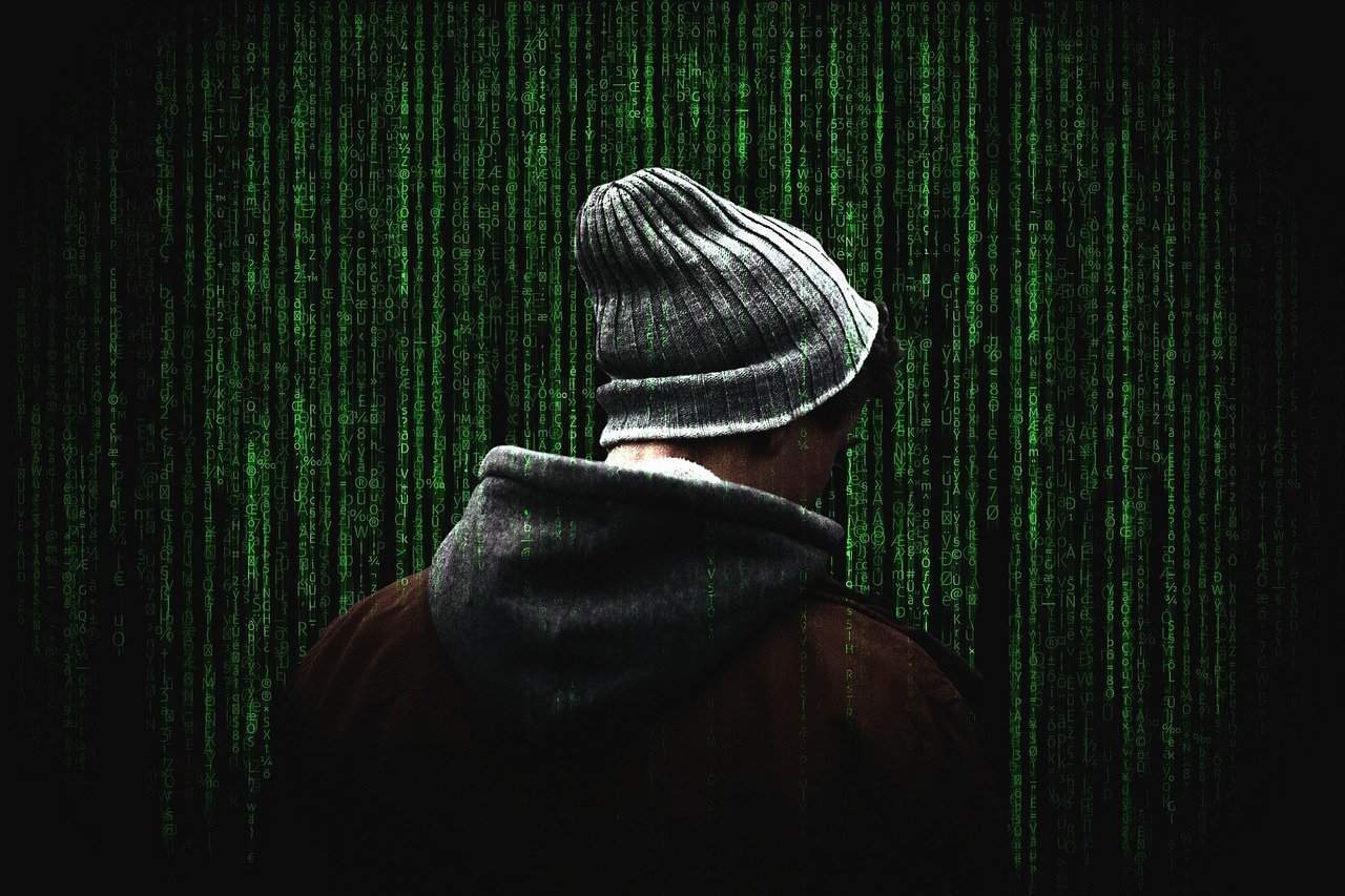 Back view of man's head wearing beanie with green computer text in background