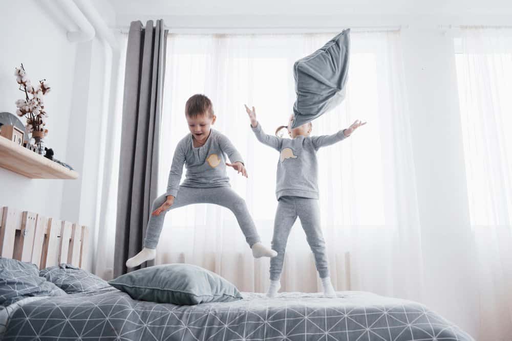 Two kids jumping and playing on the bed