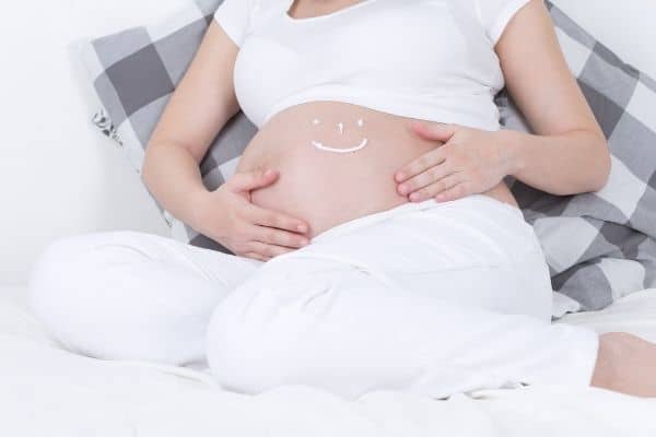 Smiley drawn with stretch mark cream on pregnant woman's belly