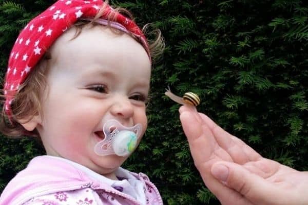 Happy baby with dummy looking at a cute snail