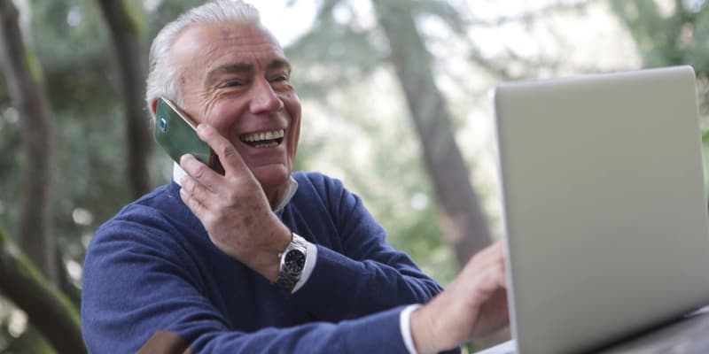 Elderly man talking on the phone while using a laptop