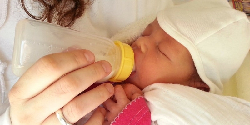 Mother using baby bottle to feed newborn baby