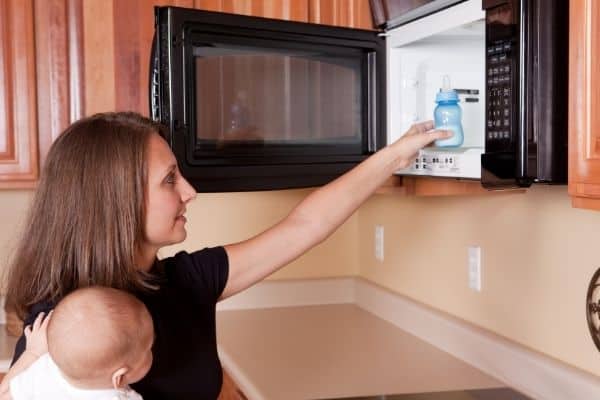 Woman with baby warming baby bottle in microwave