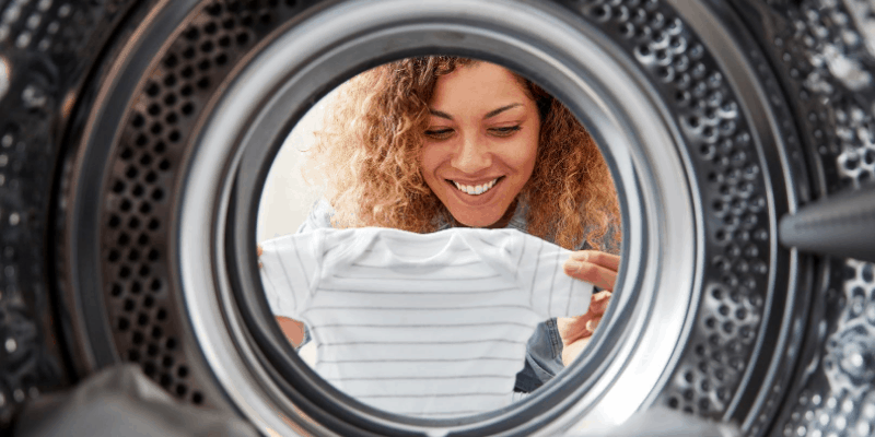 Mother holding up baby cloth near a washing machine