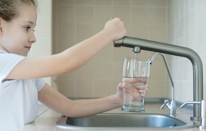 A girl using an in-line reverse osmosis water filter system at home