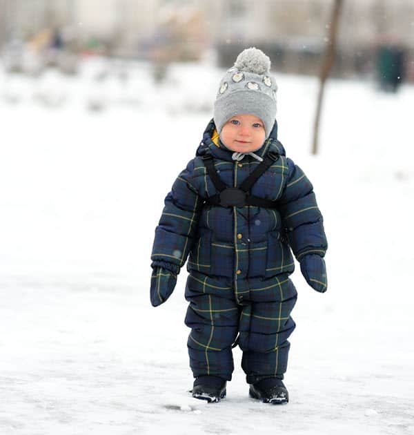 Cute baby in beanie and puffer jacket standing on wintery ice