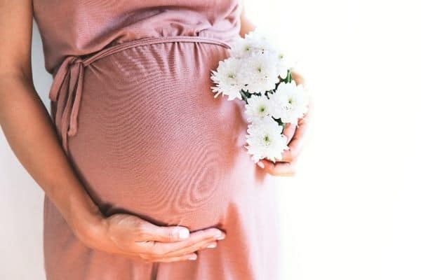 Pregnant woman in pink dress holding white flowers