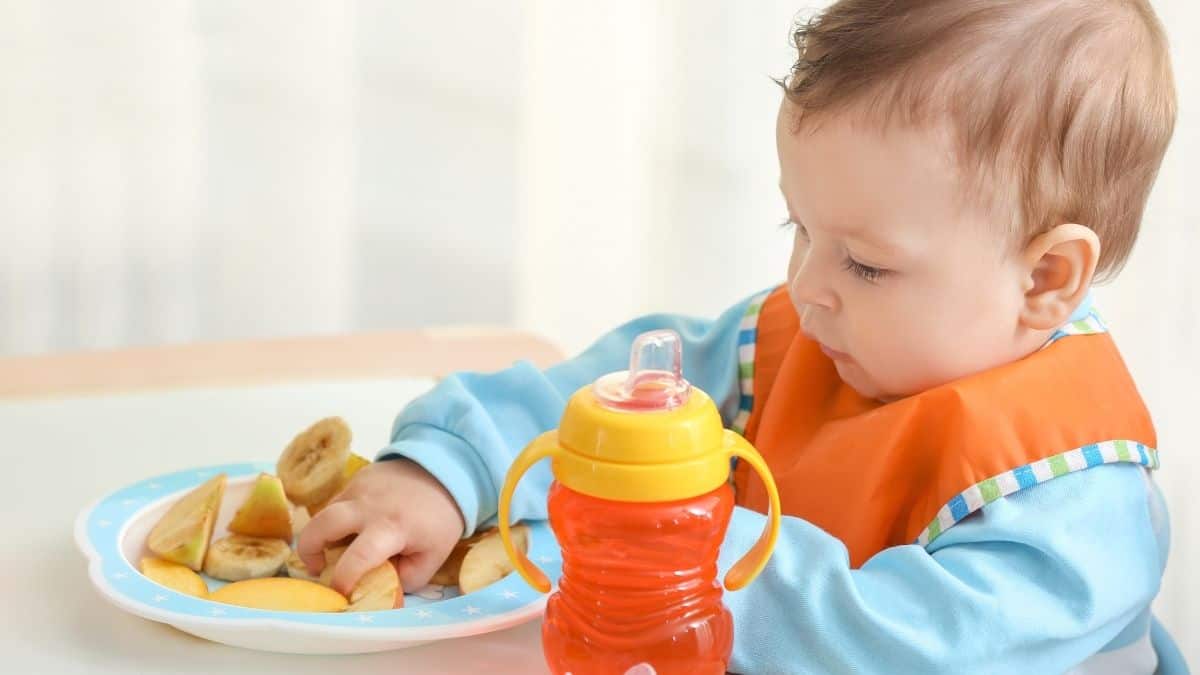 Adorable kid with orange sippy cup and bananas
