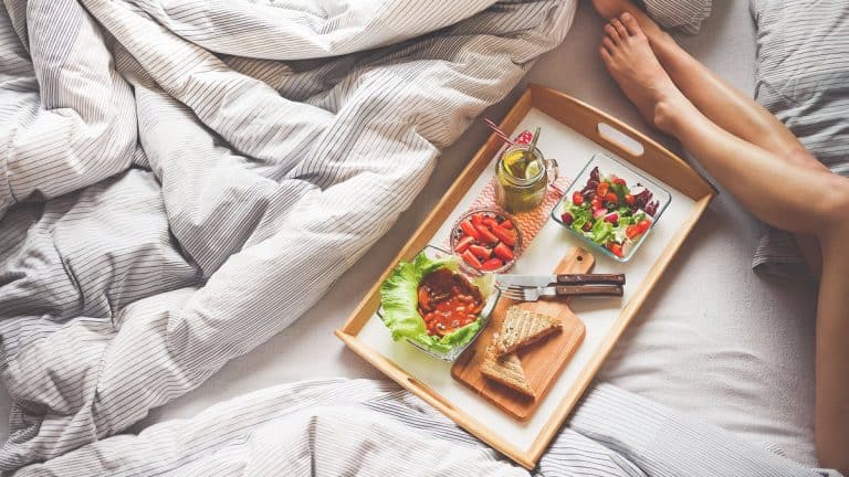 Tray with breakfast food on bed next to womans legs
