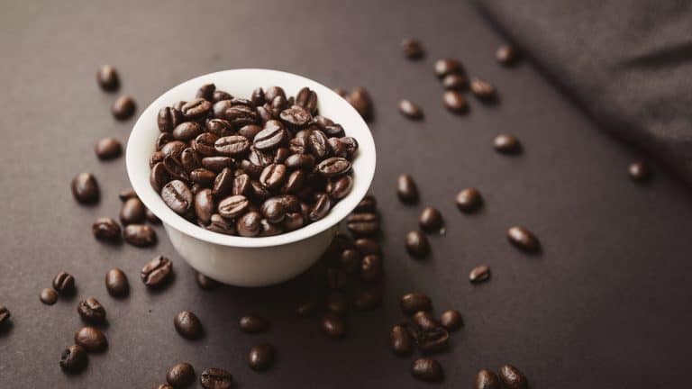 Coffee beans in a small white cup and scattered across a table