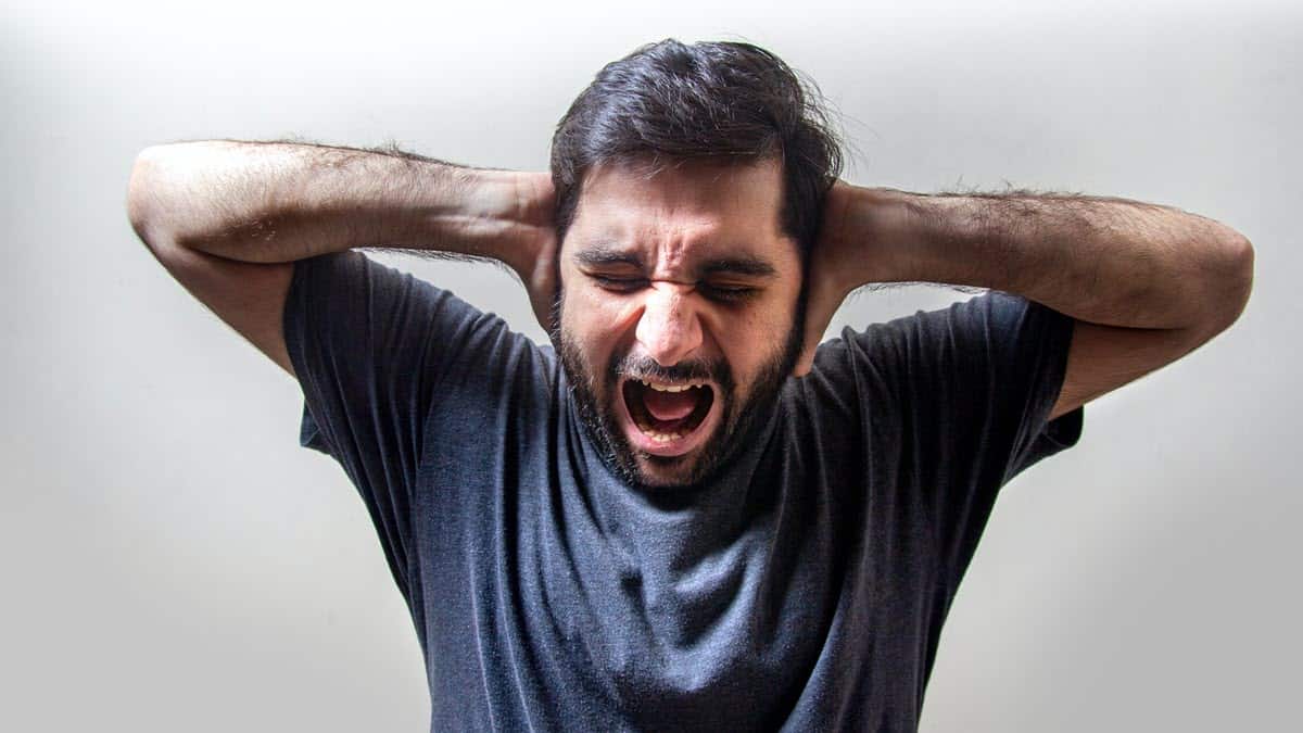 Man holding hands over ears with pained expression on face