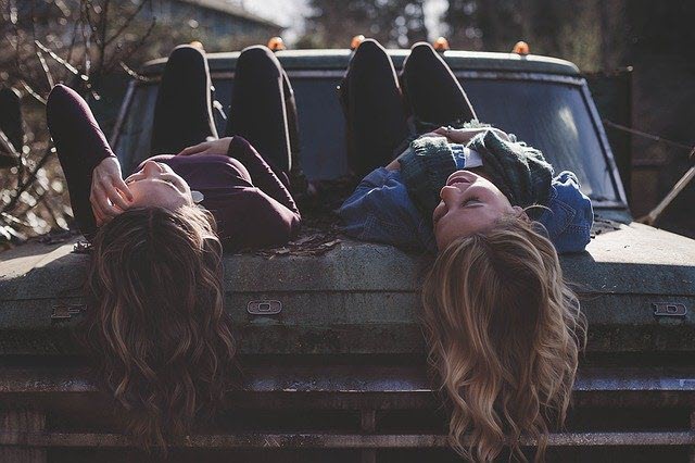 Two female friends with long hair lying on bonnet of classic car