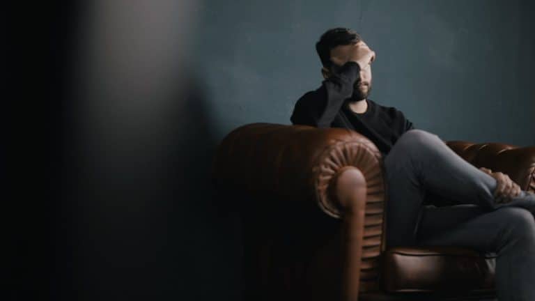 Man sitting on leather sofa with hand against forehead