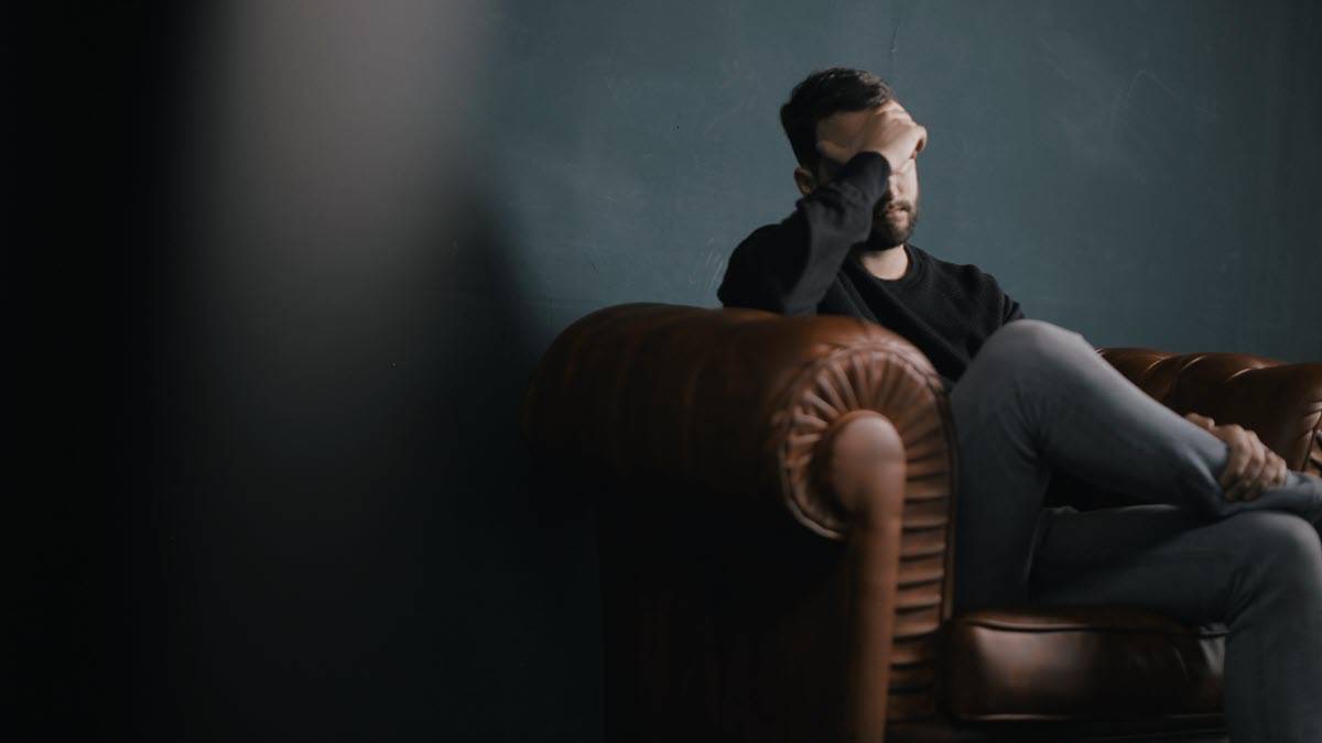 Man sitting on leather sofa with hand against forehead