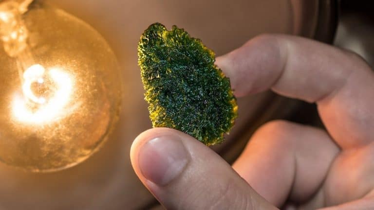 Moldavite held between thumb and forefinger near incandescent light globe