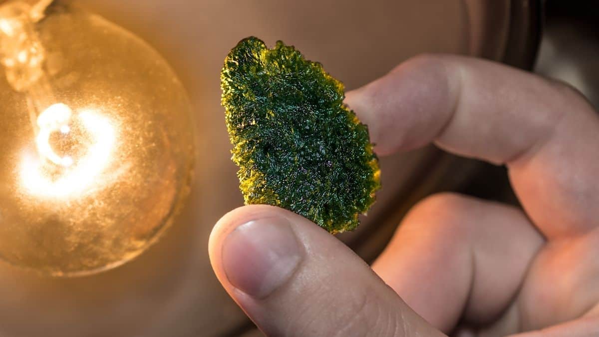 Moldavite held between thumb and forefinger near incandescent light globe