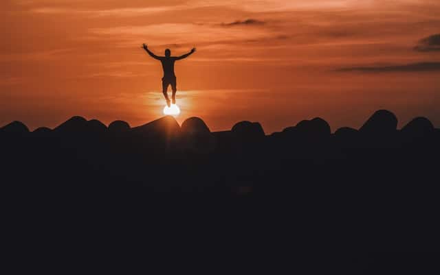 Silhouette of man jumping with sun low on horizon in background