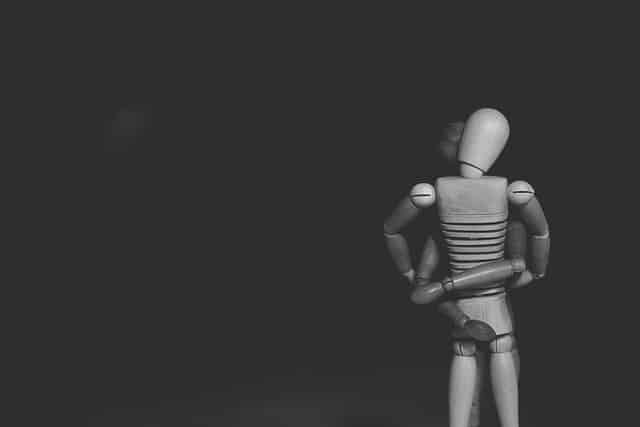 Two wooden mannequins embracing against black background