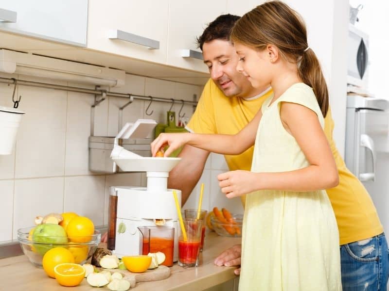 Father and daughter making fruit juice with a juicing machine