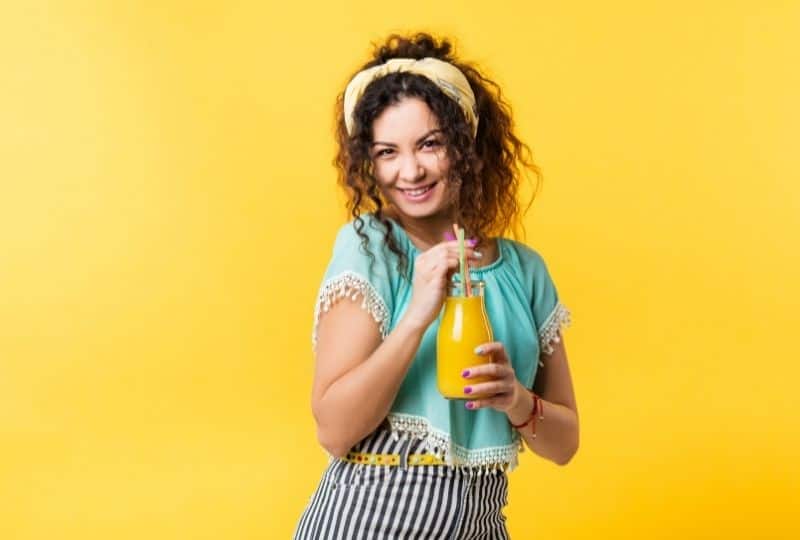Smiling woman drinking cold press juice against a yellow background