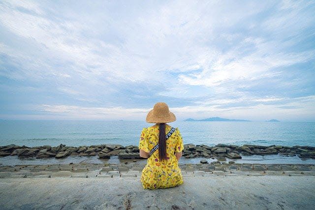 Girl in yellow dress faced away looking at ocean