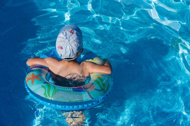 Child in swimming cap using inflatable toy in a clean swimming pool