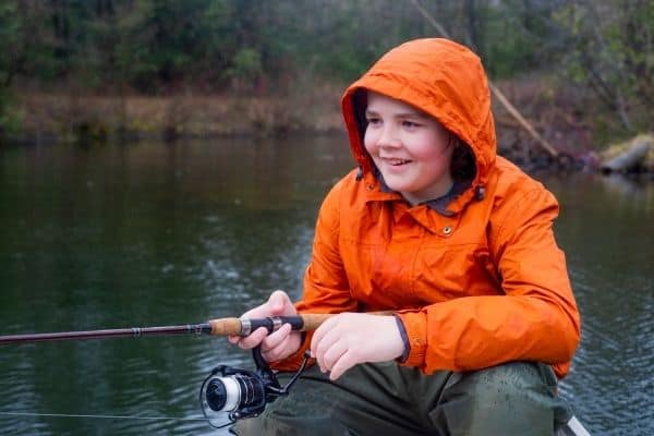 a boy in an orange jacket fishing