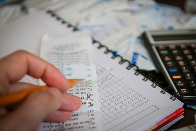 Hand holding pencil near a receipt and calculator - forming a household budget