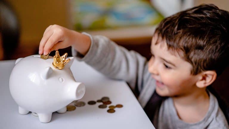 Happy young boy saving money in a white piggy bank