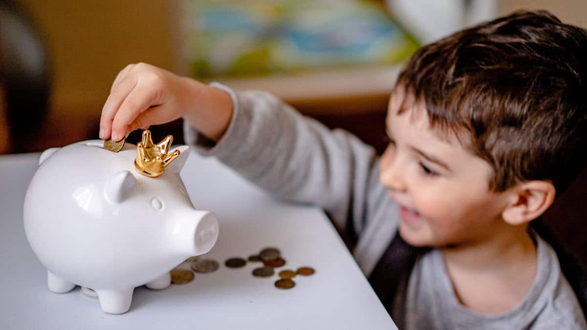 Happy young boy saving money in a white piggy bank