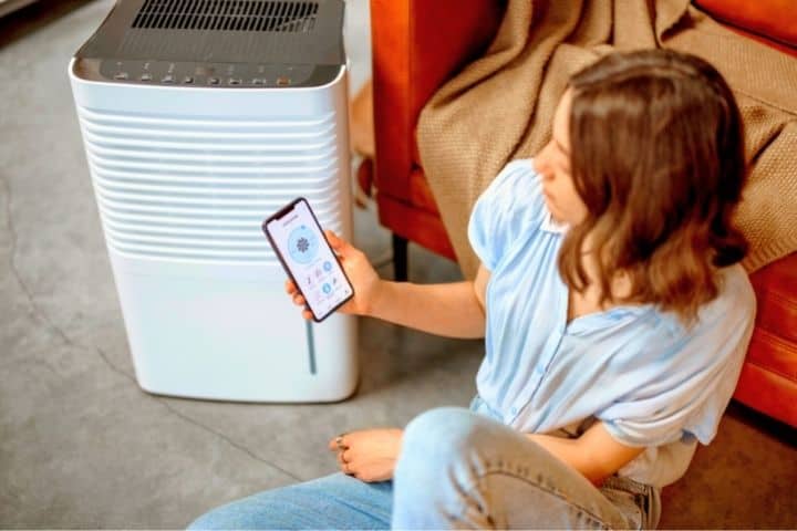 Girl Sits With Phone Next To Dehumidifier 